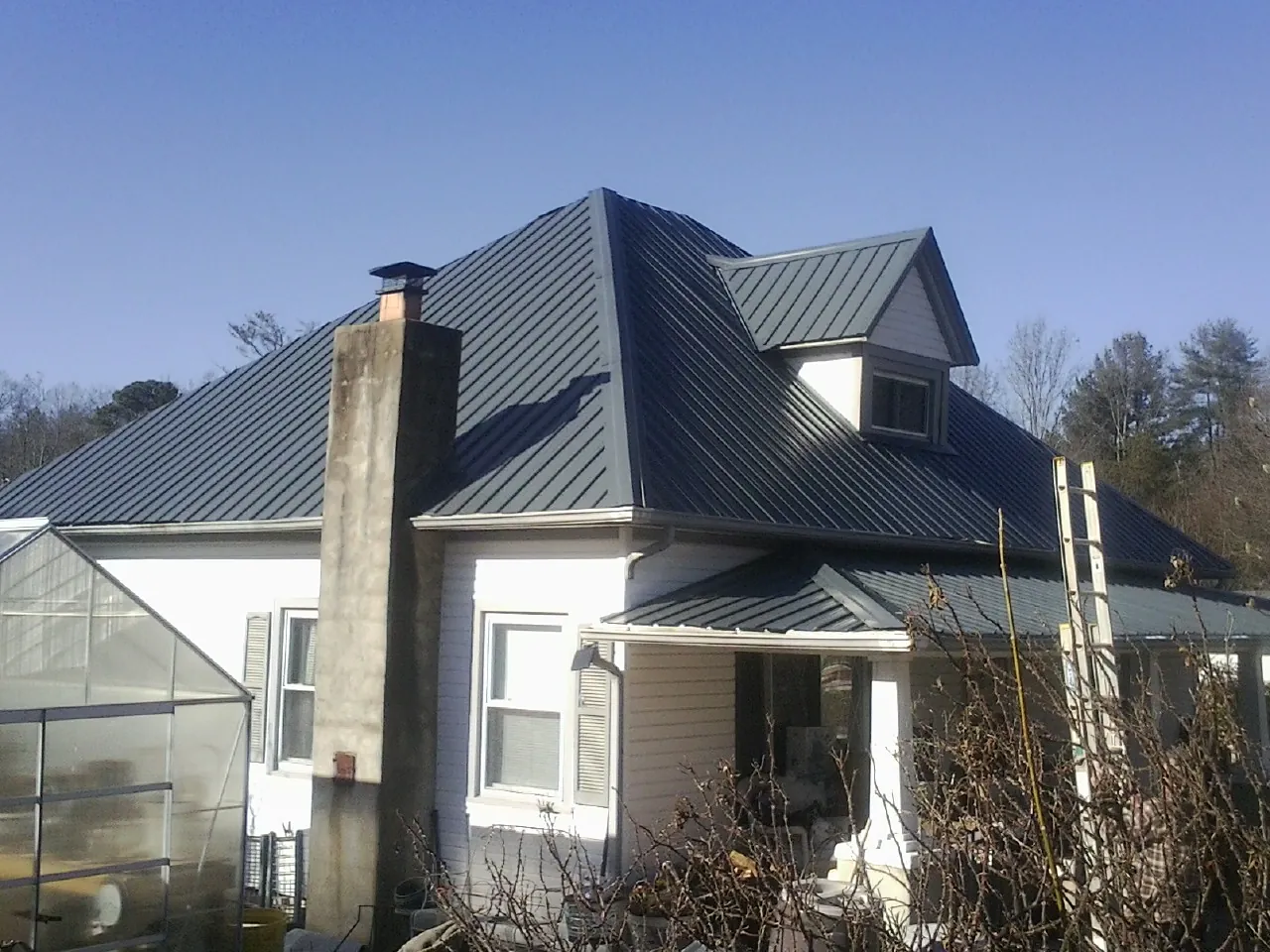 Dark blue standing seam metal roof on a white farmhouse with dormer — Slate & Tile Roof Repair by Roofing Brothers in Unityville