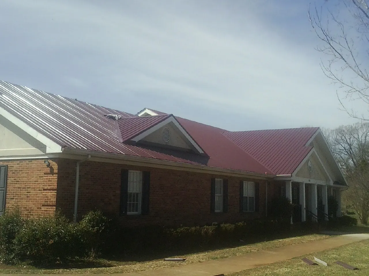 Red metal roof with gabled entries on a long brick building, from a Hail Damage Roof Repair job in Unityville