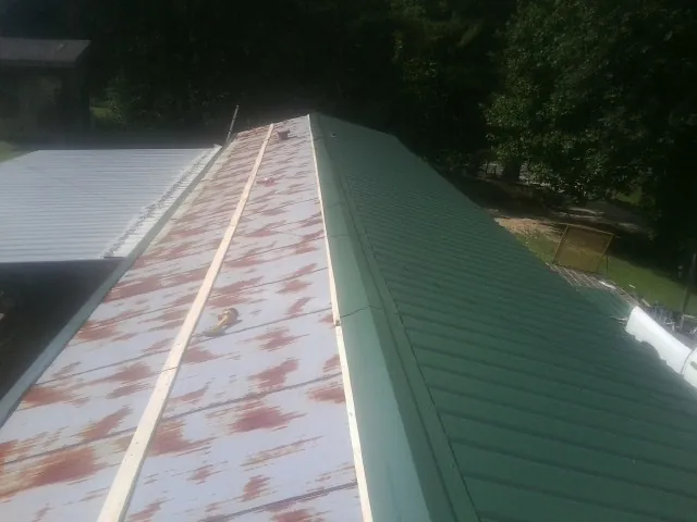 Old rusted panels beside newly installed green metal roofing — Wind Damage Roof Repair by Roofing Brothers in Unityville