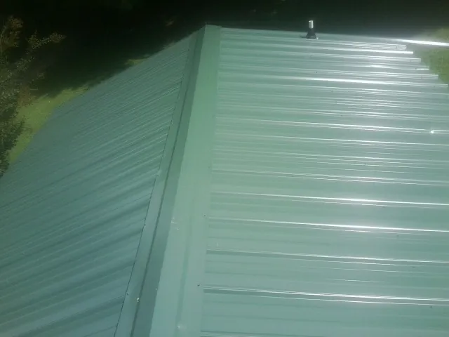 New green metal panels meeting at the ridge of a roof — Flat Roof Repair work by our crew in Unityville