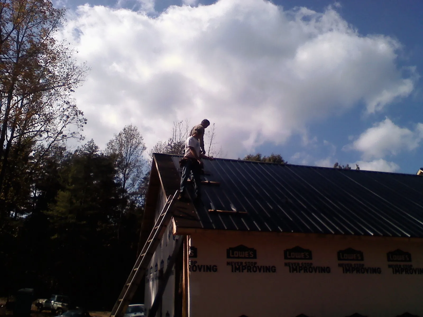 Roofer fastening dark metal panels high against a cloudy sky, from a Roof Inspection job in Unityville